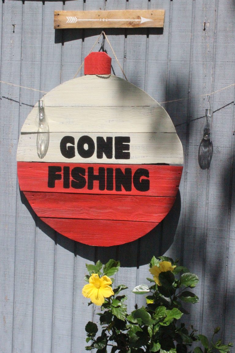 A charming rustic sign with a fishing theme, hanging outdoors. Un panneau rustique charmant avec un thème de pêche, suspendu à l'extérieur.