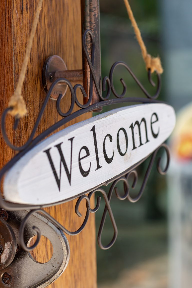 Charming close-up of a rustic welcome sign hanging on a wooden door, creating a warm inviting ambiance. Gros plan charmant d'un panneau de bienvenue rustique suspendu à une porte en bois, créant une ambiance chaleureuse et accueillante.