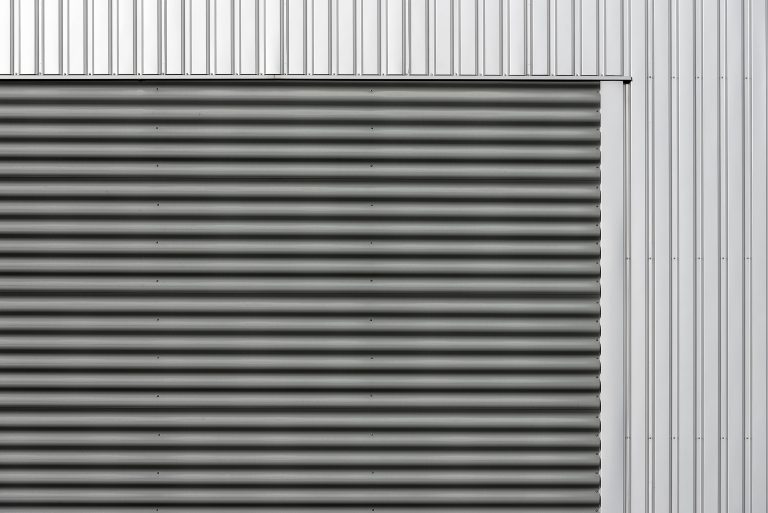 Façade métallique minimaliste avec panneaux verticaux ondulés et lisses en tons gris et argent.