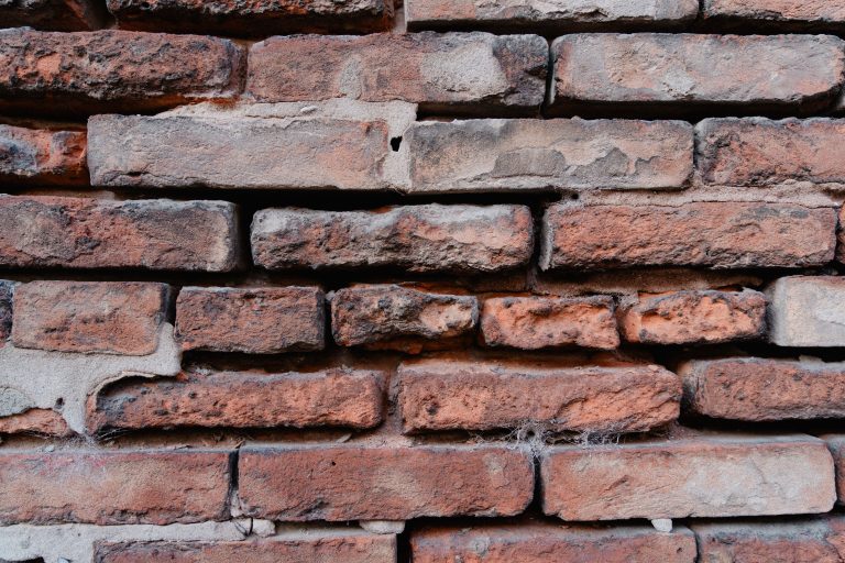 Detailed close-up view of an aged red brick wall showcasing texture and rustic appearance. Vue rapprochée détaillée d'un mur de briques rouges vieillis mettant en évidence la texture et l'apparence rustique.