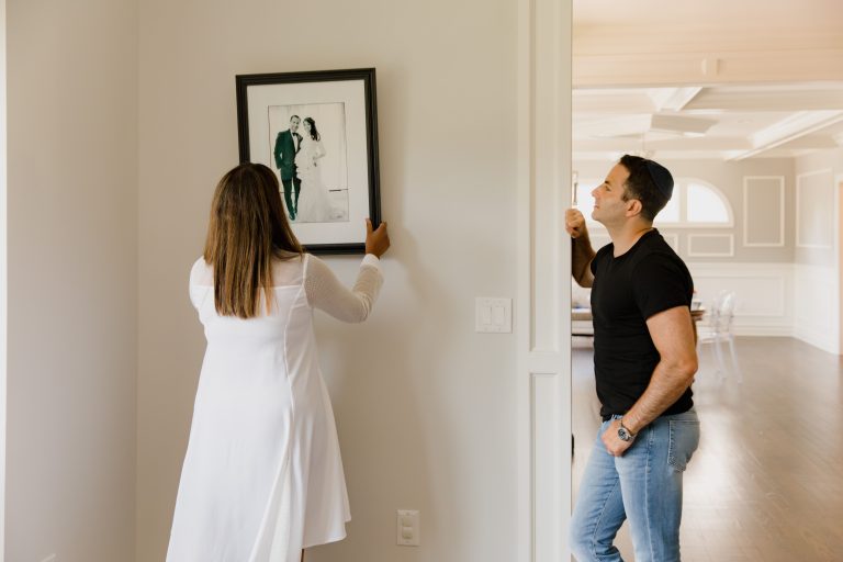 A couple decorates their modern home by hanging a framed photograph on the wall. Un couple décore sa maison moderne en accrochant une photographie encadrée au mur.