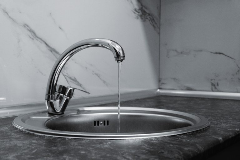 Chrome faucet with running water in a modern kitchen with marble countertop. Robinet chromé avec eau courante dans une cuisine moderne avec plan de travail en marbre.